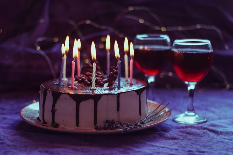 Birthday cake with candles and wine glasses.