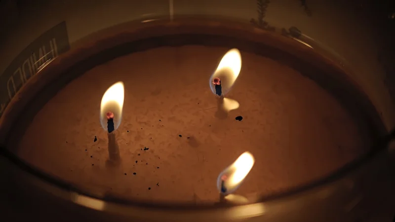 Three lit candles burning in a wax container.